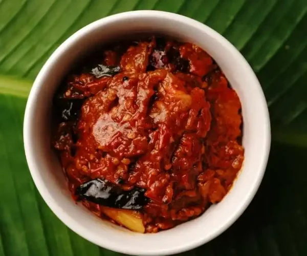 A cup full of DNachiys Tomato Pickle on a banana leaf